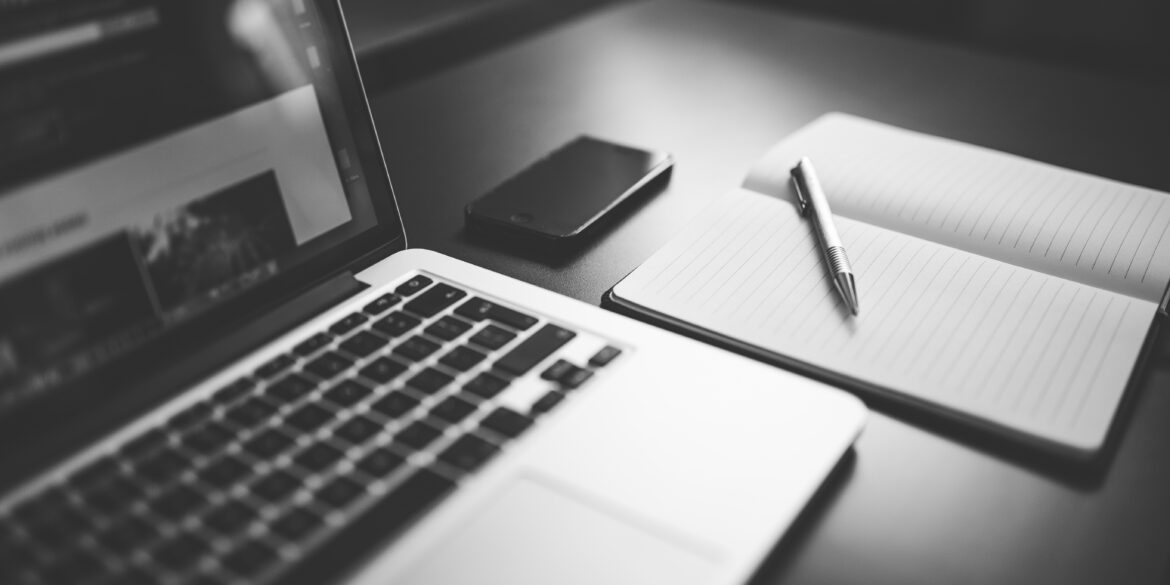 un computer un quaderno e una penna su un tavolo, foto in bianco e nero