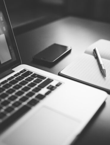 un computer un quaderno e una penna su un tavolo, foto in bianco e nero