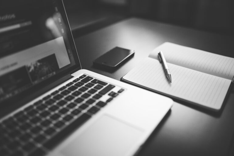 un computer un quaderno e una penna su un tavolo, foto in bianco e nero